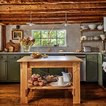 a kitchen with green lower cabinets and low wooden ceiling beams and a wood island in the middle