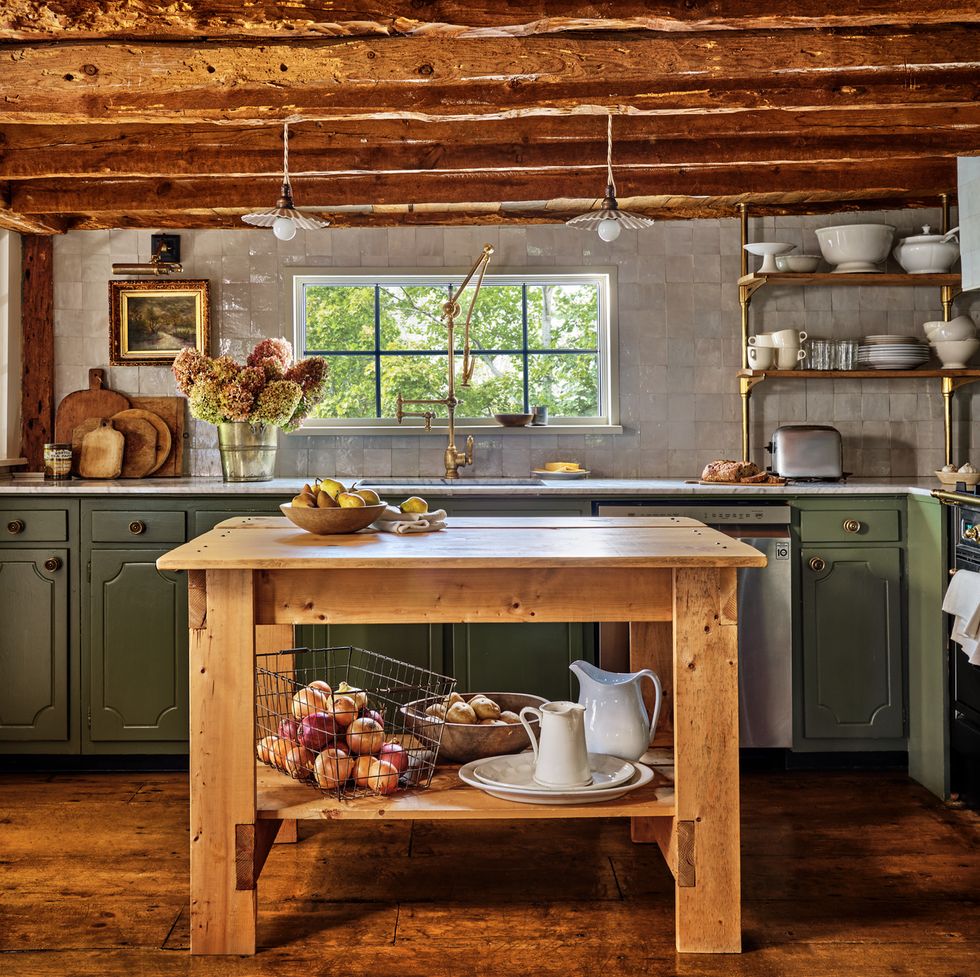 a kitchen with green lower cabinets and low wooden ceiling beams and a wood island in the middle