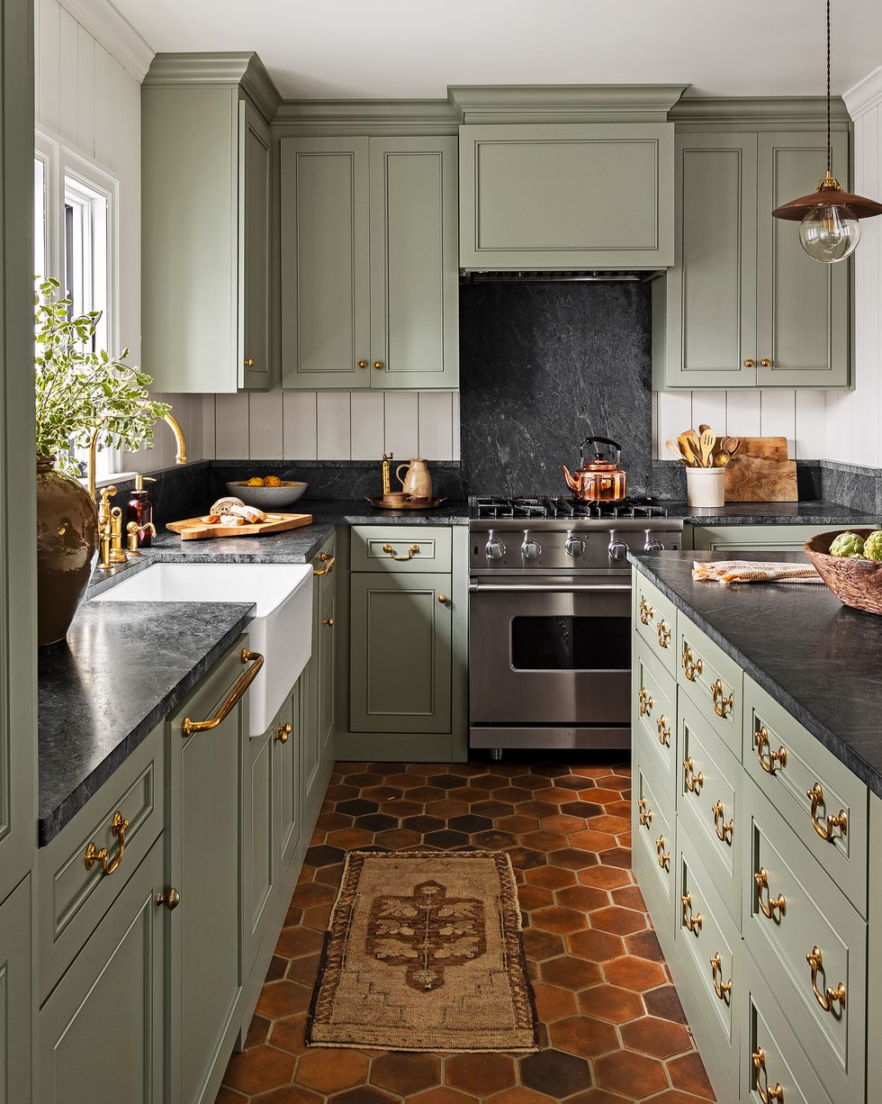 green kitchen cabinets with a warm terra cotta tile floor and black countertops