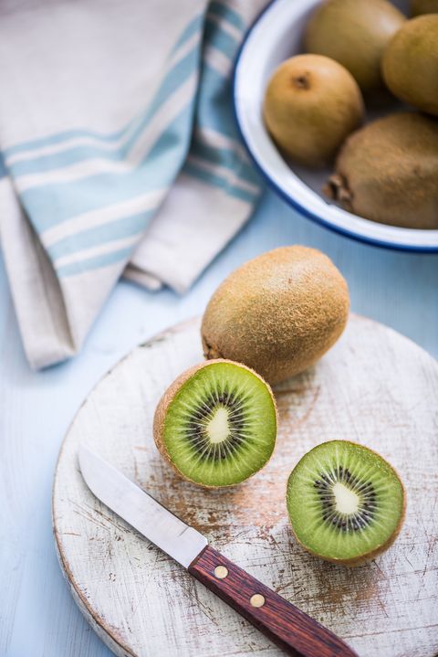 green ripe kiwi fruit on a wooden cutting board with a knife