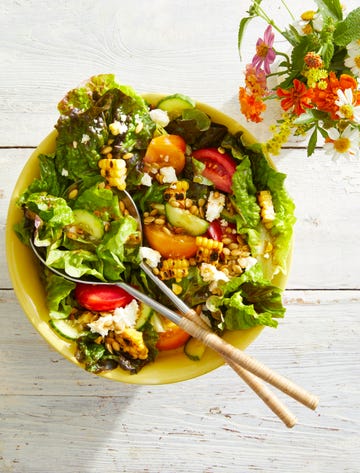 a green salad with pepitas and queso fresco in a yellow bowl with two serving spoons