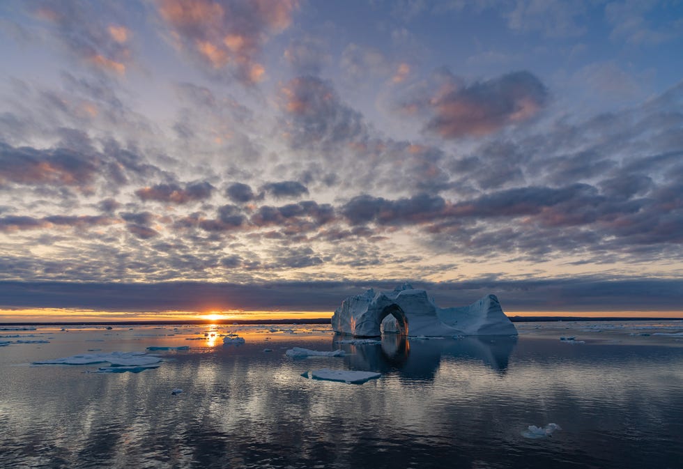 icebergs in a body of water under a cloudy sky at sunset