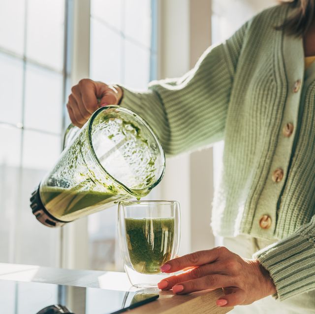 women wearing green cardigan puts greens smoothie into glass