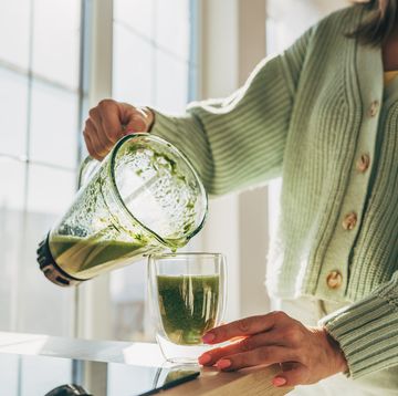 women wearing green cardigan puts greens smoothie into glass