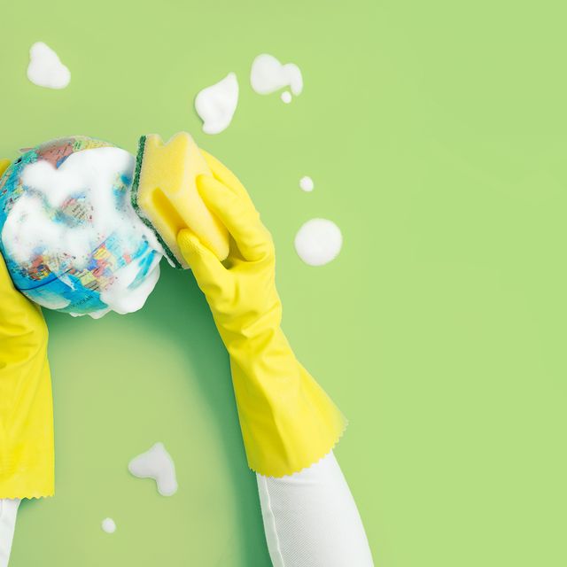 hand with protective rubber glove cleaning a globe model with soap and cleaning sponge on green background