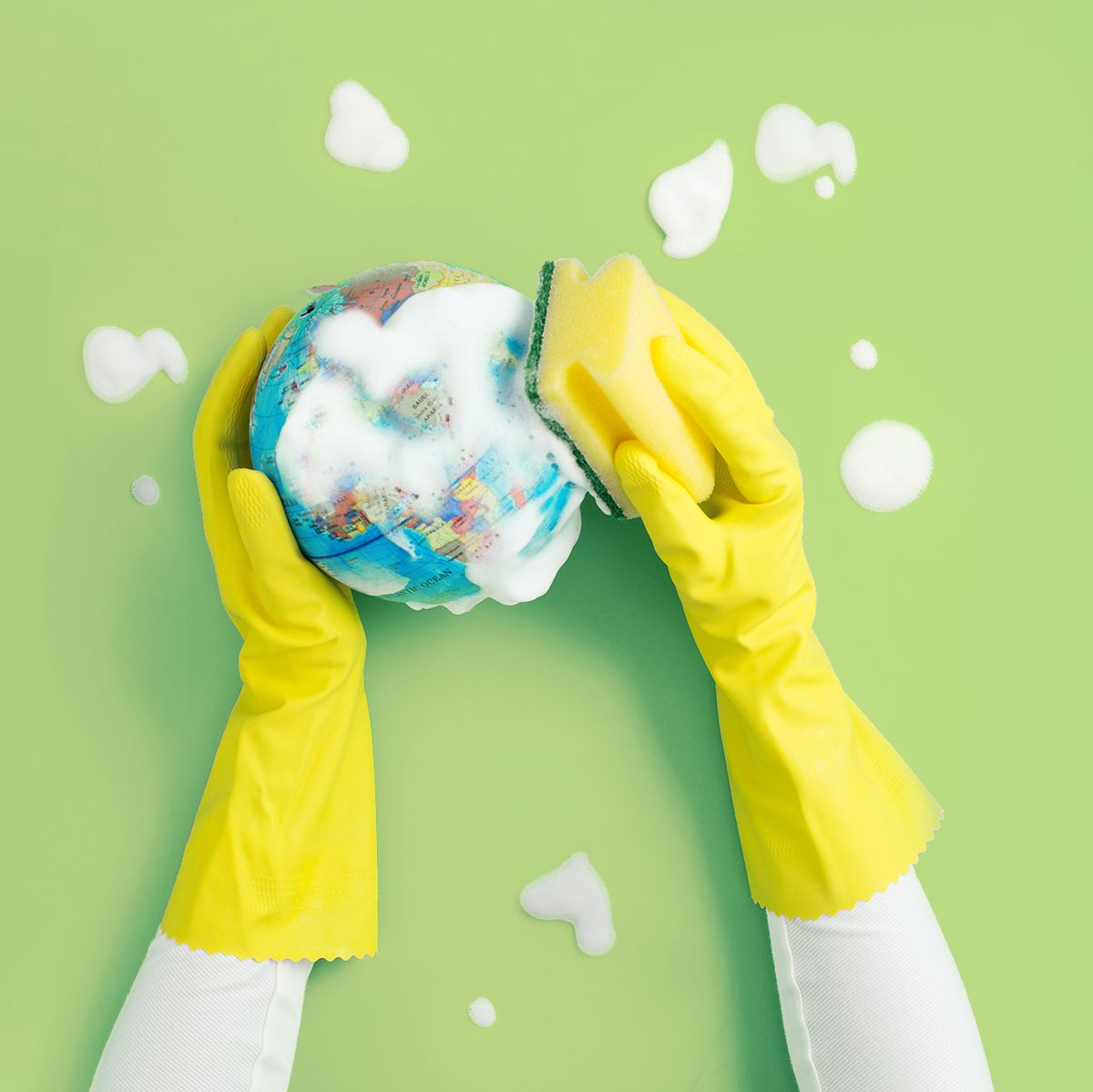 hand with protective rubber glove cleaning a globe model with soap and cleaning sponge on green background