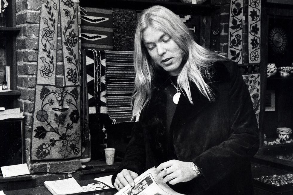 gregg allman wearing and black coat and looking at a newspaper inside a jewelry shop