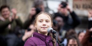 greta thunberg standing at a podium wearing a purple down coat with braided hair