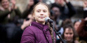 greta thunberg standing at a podium wearing a purple down coat with braided hair