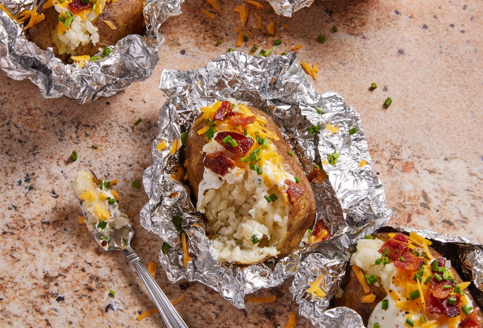 grilled baked potatoes in foil topped with sour cream, bacon, chives, and cheese