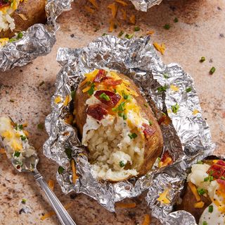 grilled baked potatoes in foil topped with sour cream, bacon, chives, and cheese