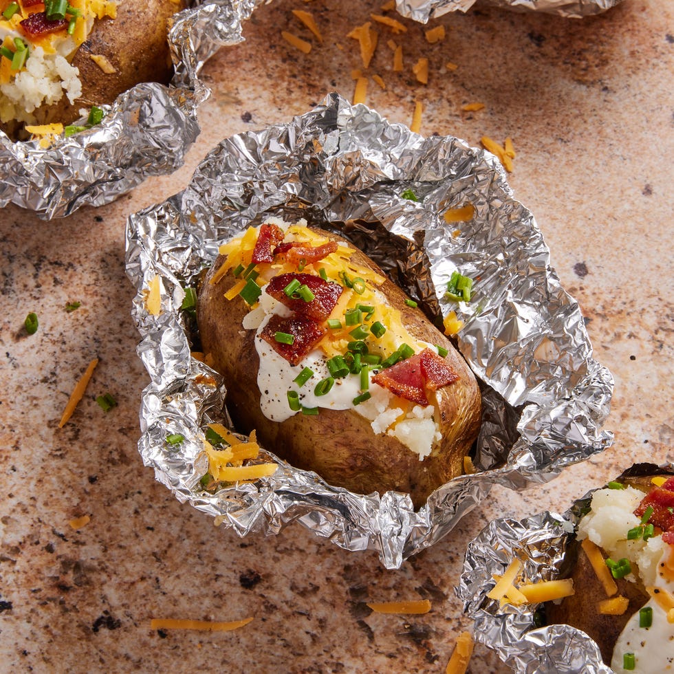 grilled baked potatoes in foil topped with bacon, sour cream, cheese, and chives