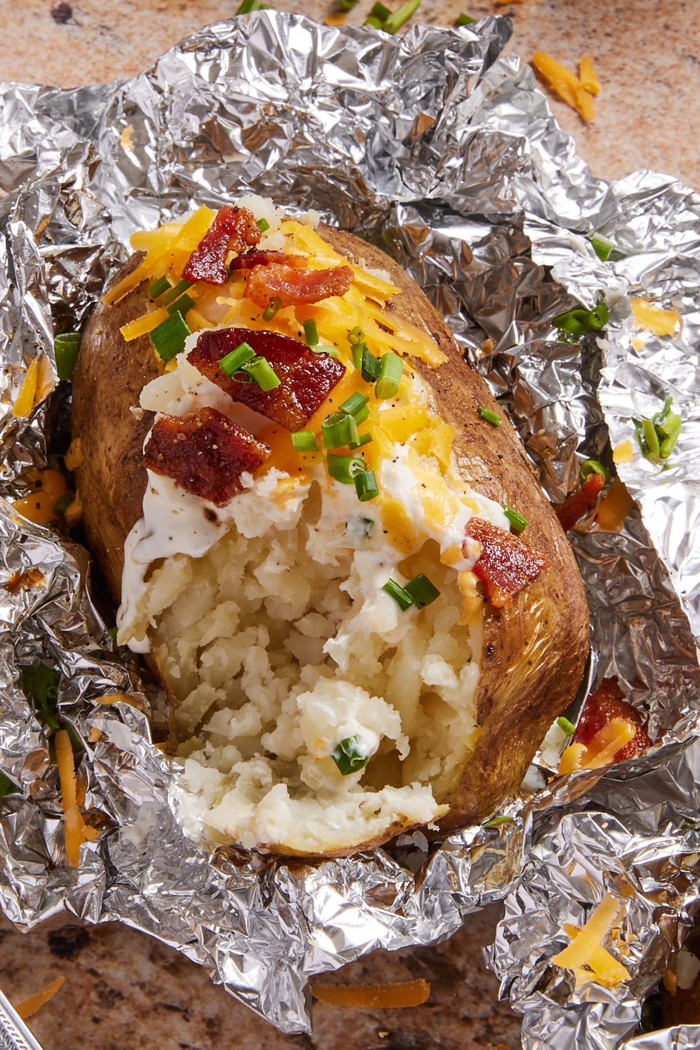 grilled baked potatoes in foil topped with bacon, sour cream, cheese, and chives