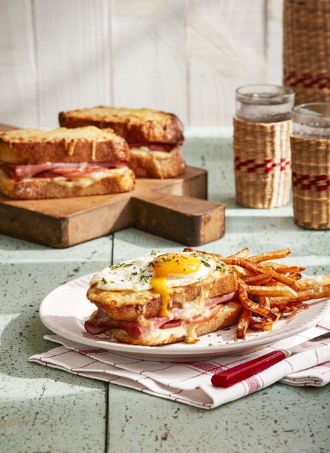 gourmet croque madames topped with sunny side up fried egg served with fries on white plate atop white and red plaid napkin