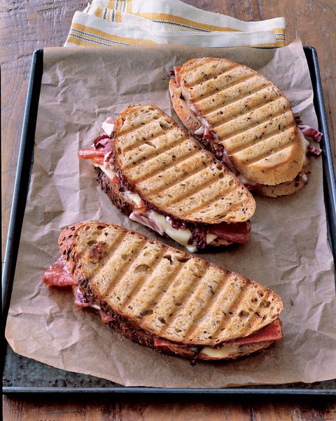 three salami and cheese paninis on rye bread on a parchment paper lined baking sheet
