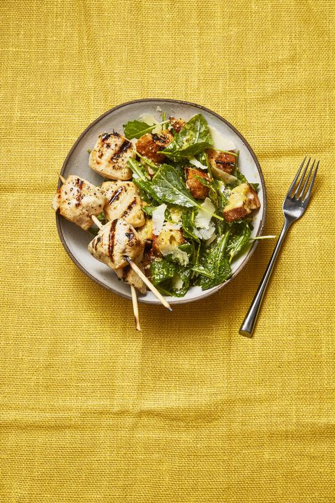 grilled chicken skewer  and kale caesar salad on a white plate