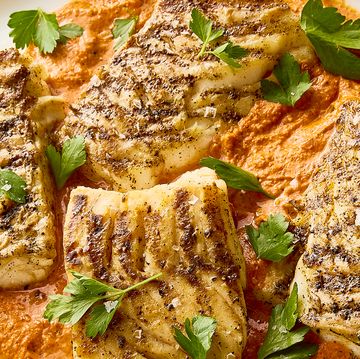 grilled cod on top of a spread of romesco sauce on a white plate topped with herbs