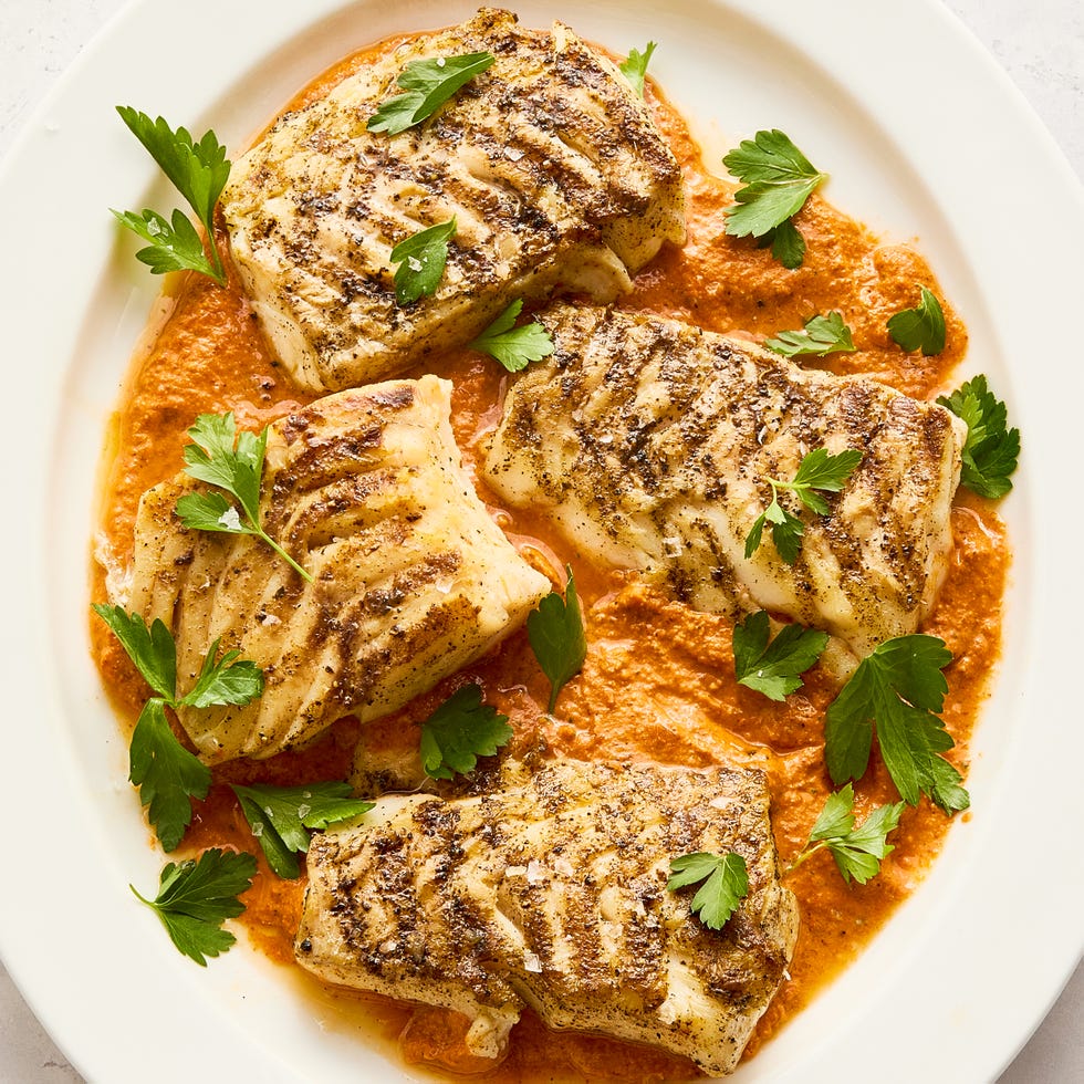grilled cod on top of a spread of romesco sauce on a white plate topped with herbs