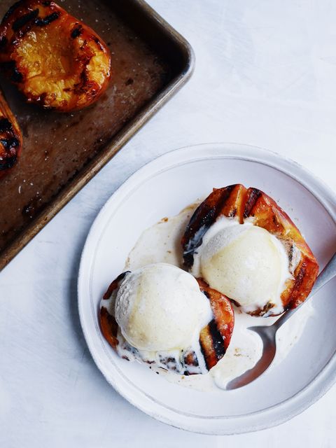 grilled peach halves in a white bowl topped with vanilla ice cream scoops