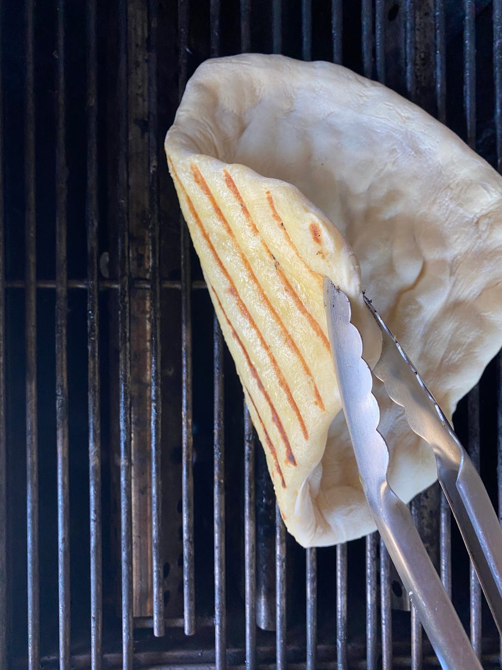 tongs holding up pizza dough on grill