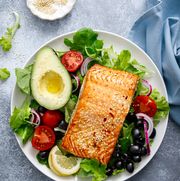 grilled salmon fish fillet and fresh vegetable salad with tomato, red onion, black olives and avocado