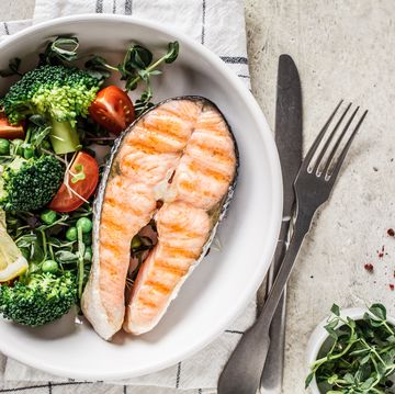 grilled salmon steak with broccoli and tomatoes in a white plate on gray background, top view, copy space diet food concept
