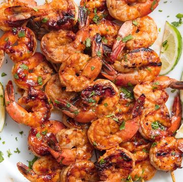 grilled shrimp on a skewer on a plate served with limes and topped with herbs