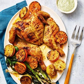 grilled spatchcock chicken with lemons and green scallions served on a white plate