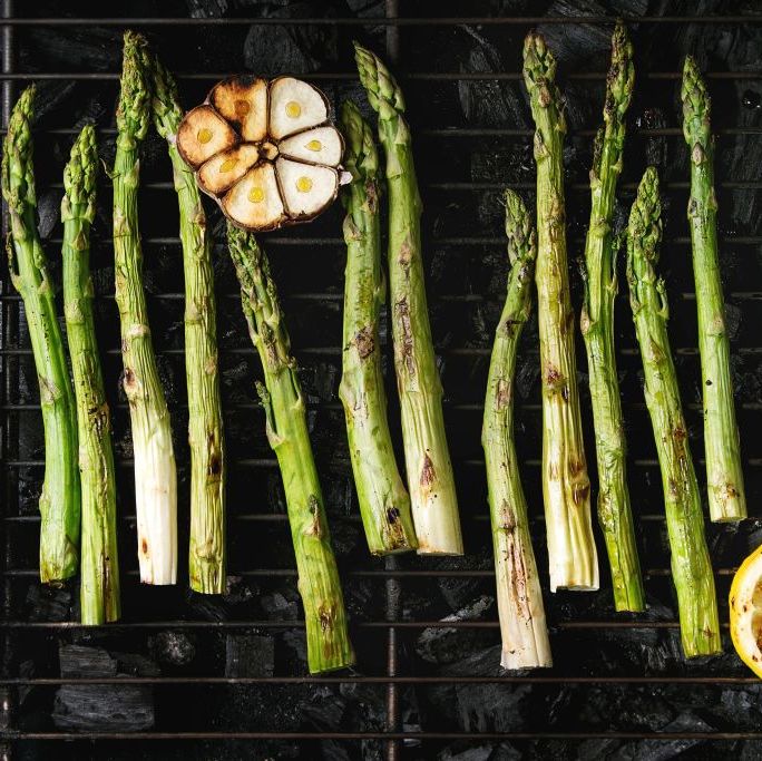 grilled vegetables green asparagus, garlic, lemon on bbq grill rack over charcoal top view, space