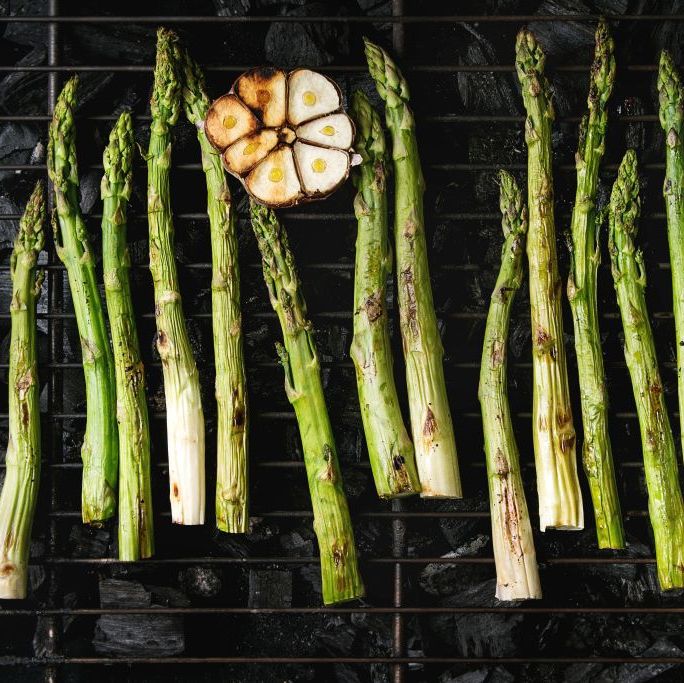 grilled vegetables green asparagus, garlic, lemon on bbq grill rack over charcoal top view, space