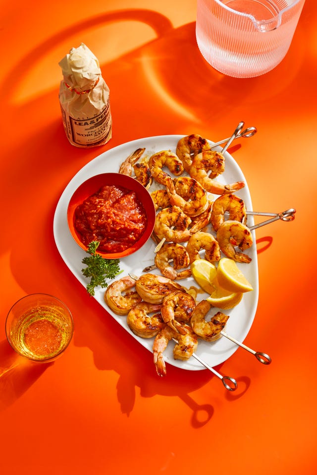 skewers of grilled shrimp on a white plate with a red dipping sauce on the side