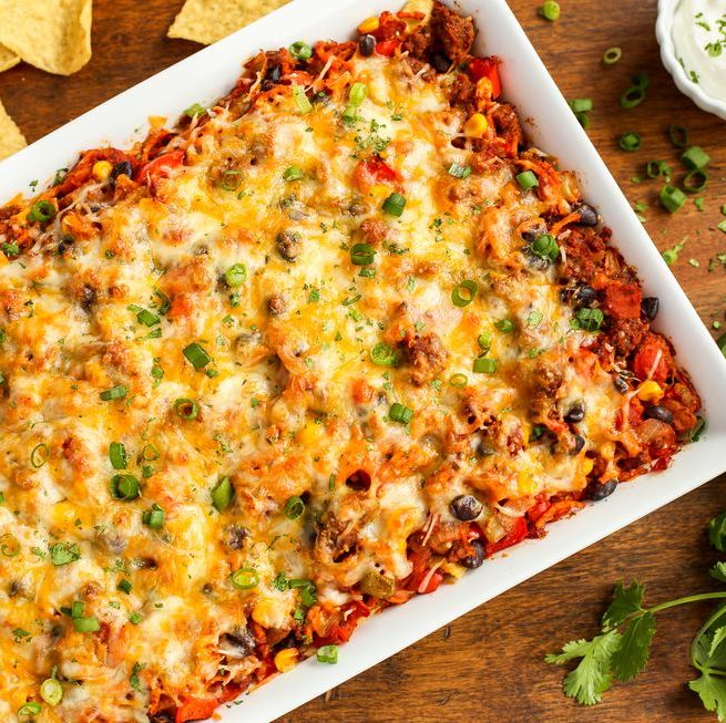 cheesy beef and sweet potato taco casserole on wood surface with herbs