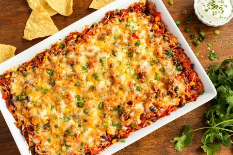 cheesy beef and sweet potato taco casserole on wood surface with herbs