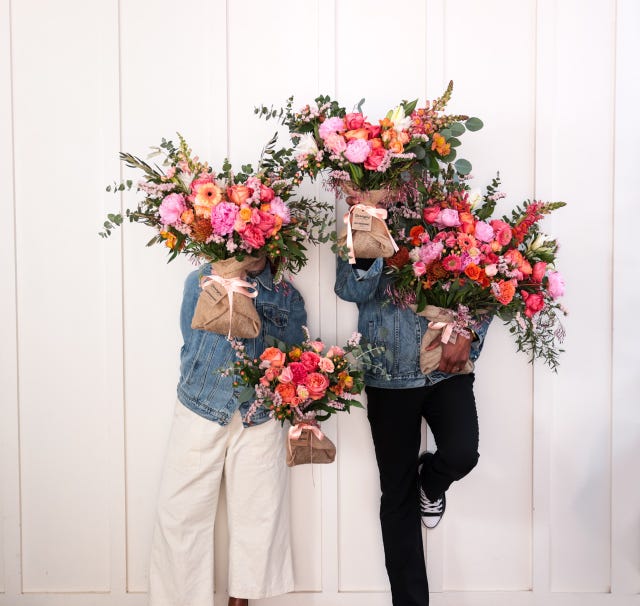 two individuals holding large floral arrangements in front of a white wall