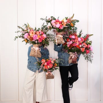 Farmgirl flowers two individuals holding large floral arrangements in front of a white wall