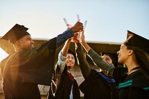 graduates holding up their diplomas while wearing cap and gowns