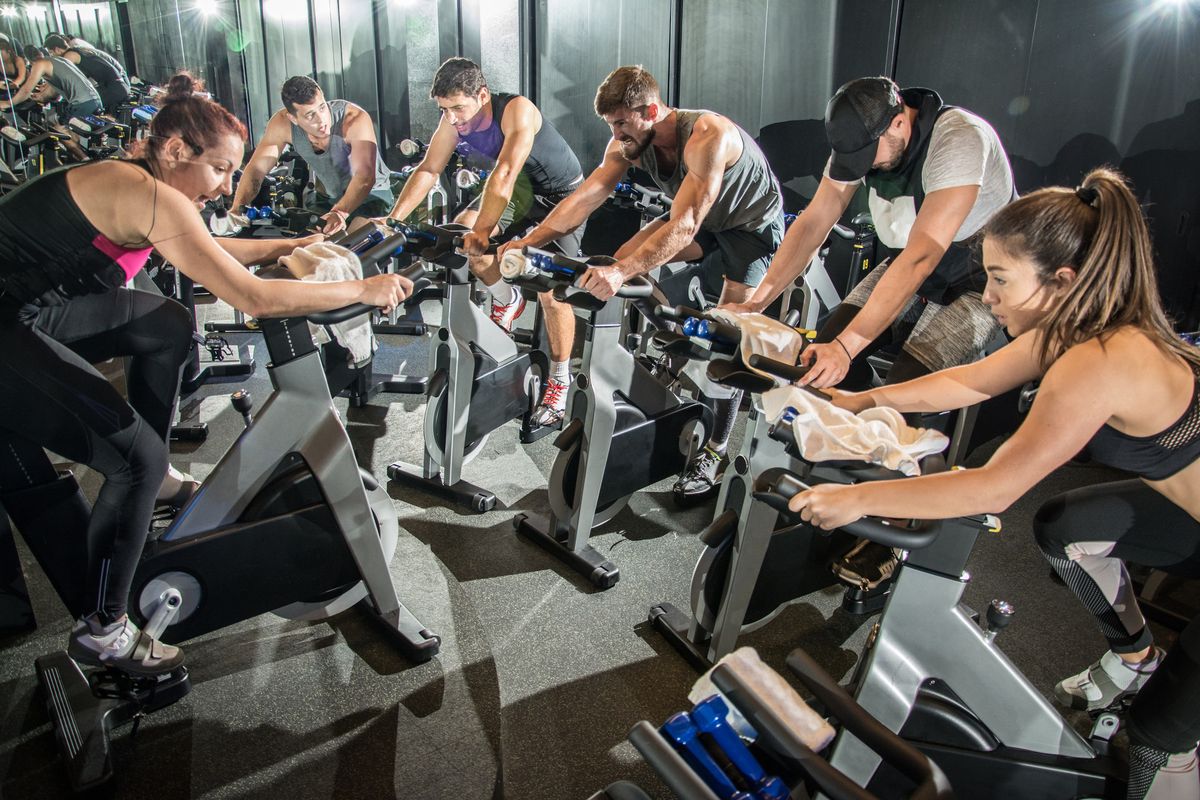 Group of fit people working out on spinning class in gym.