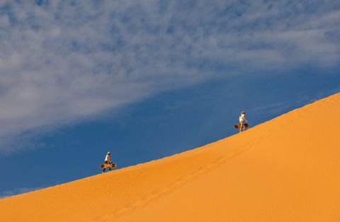 group of friends climbing a dune to sandboard in rub al khali desert, najran province, thar, saudi arabia