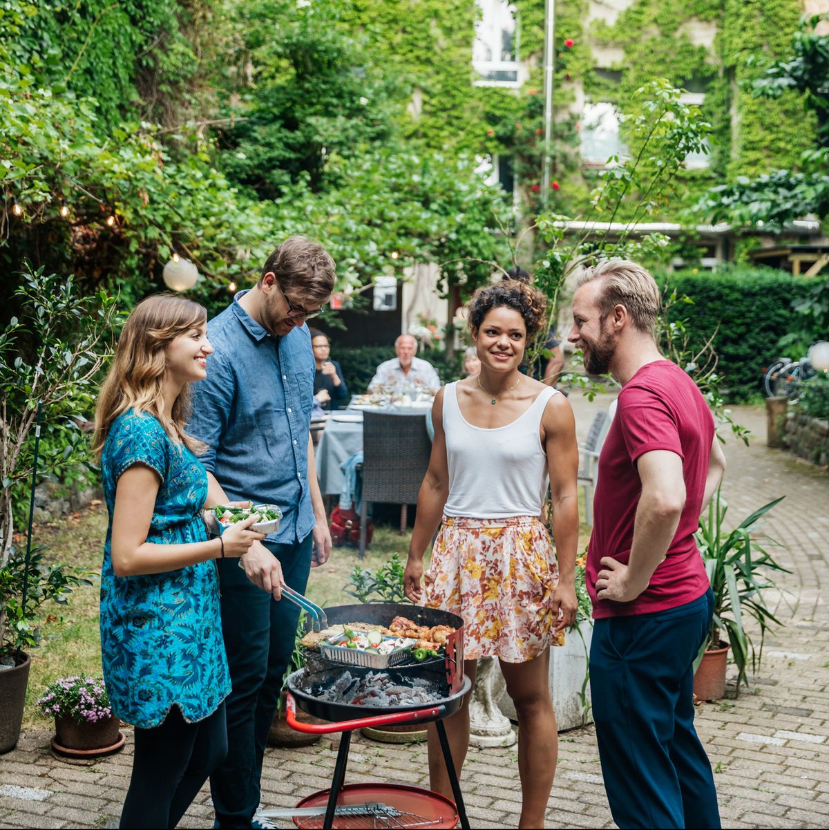 Group Of Friends Cooking On BBQ In Courtyard