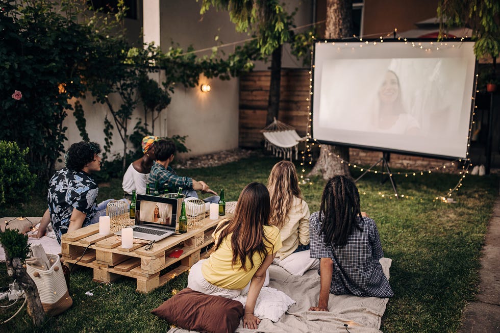 group of friends having a gathering, watching a movie on projector in the garden and hanging out