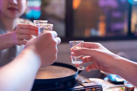 group of friends toasting glasses of soju drink alcohol beverage together in korean restaurant