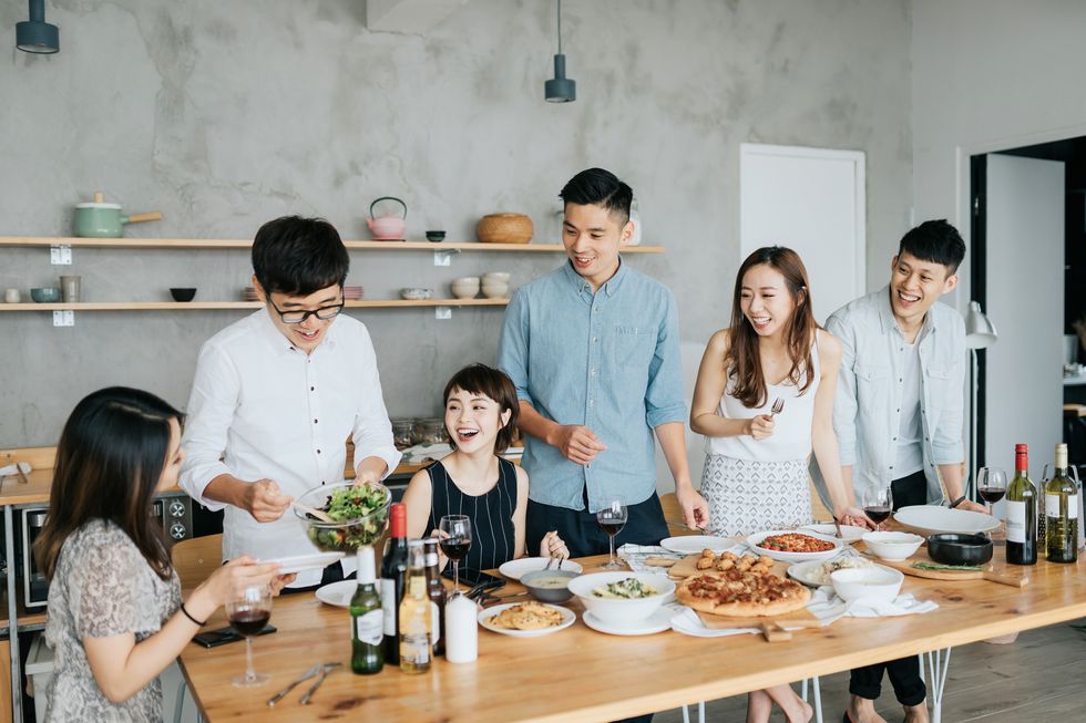 group of joyful young asian man and woman having fun, passing and sharing food across table during party