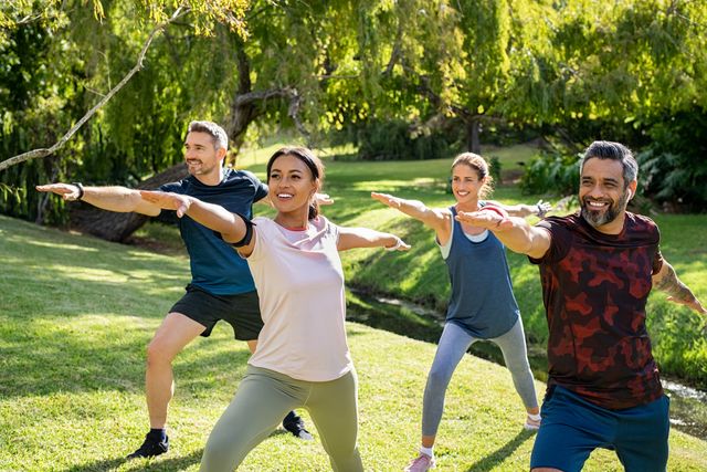 group of mature men and women stretching at park after workout