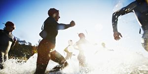 Group of triathletes running into water at sunrise