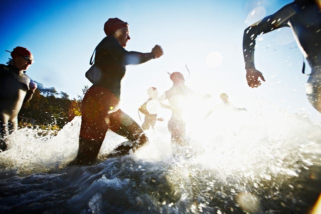 Group of triathletes running into water at sunrise