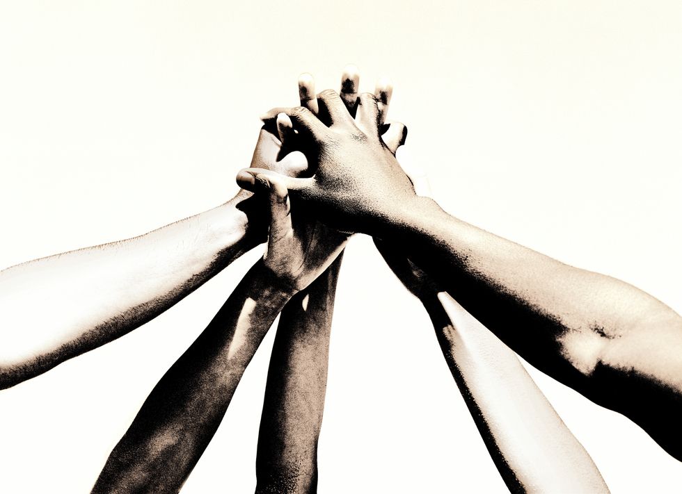 group of young people's hands clasped together toned bw