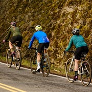 three cyclists riding uphill alongside a mountain