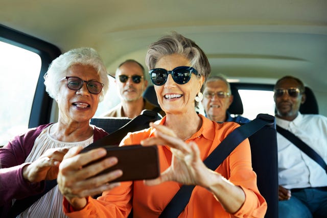 smiling woman using smart phone by friend in car males and females are traveling together during wine tour they are in casuals