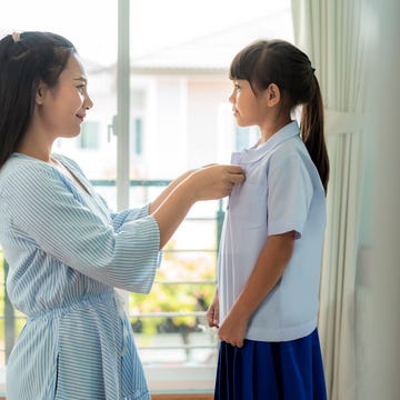 asian mother preparing primary student uniform to her little daughter for school in living room at home. the morning school routine for day in the life getting ready for school asian mother preparing primary student uniform to her little daughter for school in living room at home. the morning school routine for day in the life getting ready for school