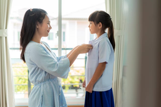 asian mother preparing primary student uniform to her little daughter for school in living room at home. the morning school routine for day in the life getting ready for school